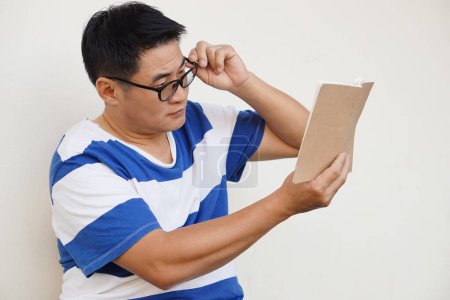 Photo for Asian middle aged man wears eyeglasses is reading book. concept , Eyesight problem. Optometry. Glasses with convex or concave lenses. Myopia.Eye disease - Royalty Free Image