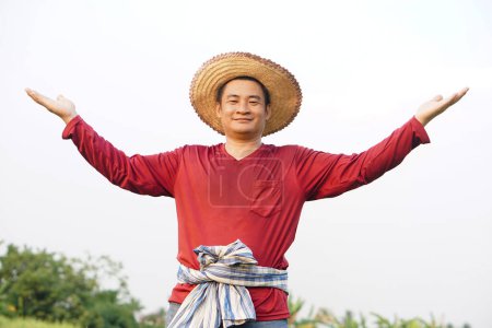 Happy Asian man farmer wears hat, red shirt, raises two hands up, feels confident. Concept, agriculture occupation, Thai farmer. Copy space of adding text or advertisement.             