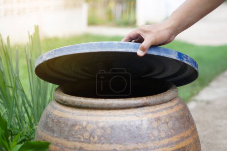 Photo for Closeup hand hold lid to cover water jar to protect from mosquito to breed inside or other  insects or dust go into water. Concept, campaign to stop mosquitoes cycle to lay eggs in water container - Royalty Free Image
