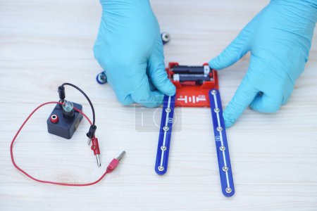 Photo for Closeup hands wear blue gloves demonstrate science experiment about electricity circuit. Concept, scientific tools for education, lab lesson. Learning by doing. Teaching aid - Royalty Free Image