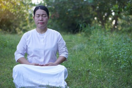 Foto de Mujer asiática budista viste traje blanco, hacer meditación sentado en el bosque tranquilo. Concepto, cultura de la fe. Actividad religiosa. Gestión de la paz mental. Concentración. - Imagen libre de derechos