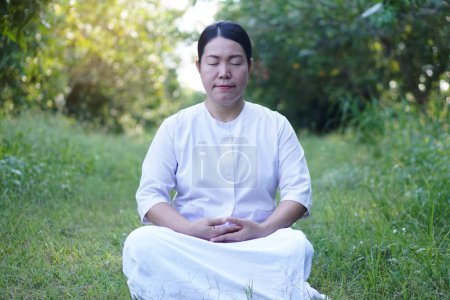 Foto de Mujer asiática budista viste traje blanco, hacer meditación sentado en el bosque tranquilo. Concepto, cultura de la fe. Actividad religiosa. Gestión de la paz mental. Concentración. - Imagen libre de derechos