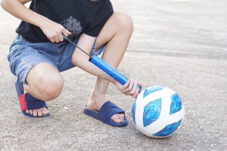 Photo for Closeup boy is pumping air into football. Concept, Portable sport equipment for inflating ball. Easy and convenient that kids can do themselves with a manual pump. - Royalty Free Image