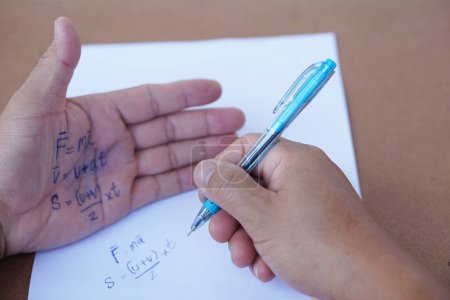 Photo for Palm with written physics formula on it during doing writing examination on paper by pen. Concept, cheat the test, Dishonest behaviour. Education assessment. - Royalty Free Image