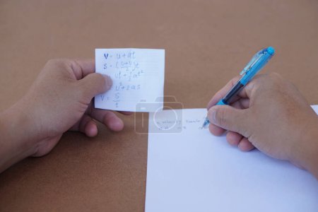 Photo for Close up hand hold small piece of paper with written fomular and another hand is writing on paper. Concept, cheat the test. Dishonest behaviour. Education assessment. - Royalty Free Image