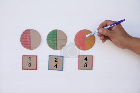 Math teaching materials about fraction. Hand hold pen to point at circle paper to show parts of color separation. Concept, education. DIY craft as teaching aid in Math subject.          