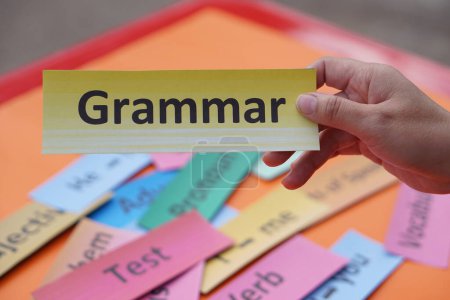 Close up student hands hold paper word card with text Grammar. Concept, English language grammar teaching. Using word card to create for playing educational fun games or practice      