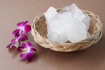 Kristallklare Aluminiumsteine oder Kaliumalaun auf Korb, mit Blumen verziert. Nützlich für Schönheits- und Wellnessbehandlungen. Körpergeruch unter den Achseln als Deo behandeln und Wasser klar machen.         
