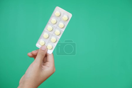 Close up hand hold blister pack of medicine pills. Green background. Concept, pharmacy, medical treatment and health care, use under doctor prescription of illness symptoms.           