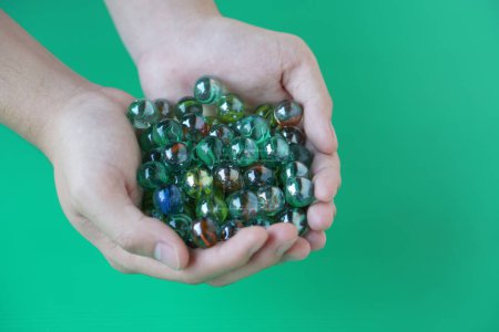 In Großaufnahme hält die Hand Murmelkugeln, kleine kugelförmige Objekte, die oft aus Glas, Ton, Stahl, Kunststoff oder Achat bestehen. Konzept. Objektverwendung als Spielzeug oder zur Basteldekoration.  