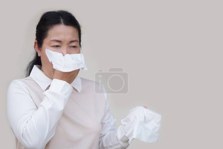 Téléchargez les photos : Femme asiatique tenir du papier de soie blanc pour couvrir sa bouche ou nettoyer le nez liquide avec de la morve de symptômes de rhume ou d'allergie. Concept, problèmes de santé. Couvrez la bouche lorsque vous toussez ou éternuez pour arrêter la propagation du germe - en image libre de droit