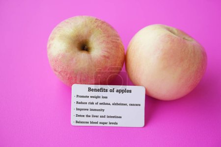 Two apples with tag of text Benefits of apples. Pink background. Concept, Apple fruits with good qualification for health. Photo for education. Teaching aid. Healthy food, fruit lesson.         