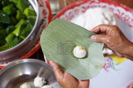 Hands hold banana leaf to wrap dough bun for cooking  Thai traditional dessert. Concept, Thai food. How to cook, step of cooking. Thai traditional lifestyle, Prepare food for cultural celebration.