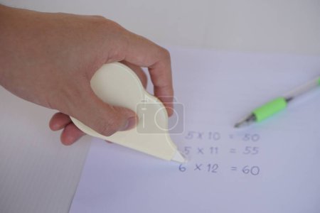 Close up hand use correction tape to erase mistake numbers on paper. Concept, education equipment for delete incorrect writing on paper. Easy and convenient to use. School supplies or office tool     