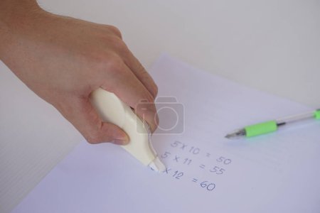 Photo for Hand use correction tape to erase incorrect numbers on paper. Concept, educational equipment, stationary item to delete or erase mistake in writing. Easy and convenient to use. - Royalty Free Image