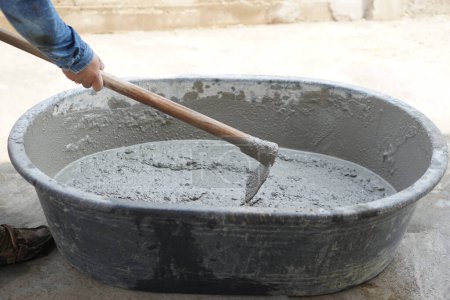 Close up worker using a hoe to mix cement powder, sand, stones in basin for mixing cement. Concept. Construction worker job. Hard working. Process of construction work with cement  