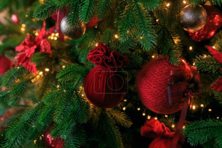Closeup of red bauble hanging from decorated Christmas tree. Christmas, holidays and seasonal greetings concepts. copy space burgundy velvet balls on green pine branches. Festive christmas background