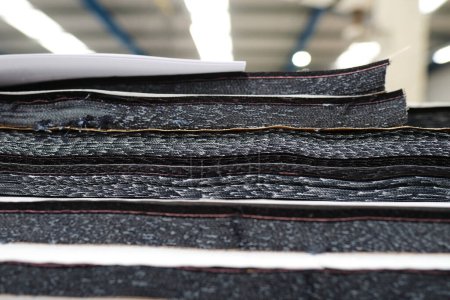 A pile of raw denim sheets fresh off a production line in a denim factory. Industrial fabric and fashion manufacture. Stylish blue denim fabric for wholesale and jeans.