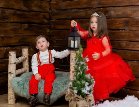 Photo for A little girl and a boy look at the Christmas candle. Wooden background. Preparing for the New Year and Christmas. A cheerful little girl looks at the Christmas lantern with a smile. Brother and - Royalty Free Image