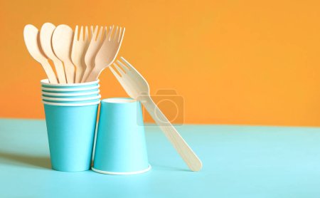 Foto de Tenedores y cucharas desechables de madera en una taza de papel azul, vista lateral. Ecológico utensilios de cocina desechables sobre fondo naranja, espacio de copia. Concepto de artículos ecológicos - Imagen libre de derechos