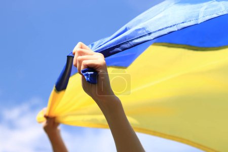 Frauenhände mit der ukrainischen Flagge gegen den Himmel. Die ukrainische Flagge flattert im Wind. Unabhängigkeitstag der Ukraine. Gelb-blaue Flagge