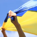 Women's hands with the Ukrainian flag against the sky. The Ukrainian flag is fluttering in the wind. Independence Day of Ukraine. Yellow-blue flag