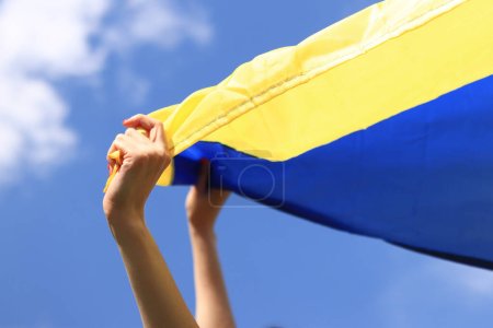 Yellow and blue flag of Ukraine in the woman's hands. Fluttering blue and yellow flag of Ukraine against sky background. Celebrate Constitution Independence flag day