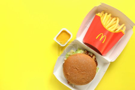 Photo for Kyiv, Ukraine - August 10, 2023: Rye burger with beef, medium portion of french fries and mustard, top view. Bright yellow background. McDonald's Corporation is the world's largest fast food restauran - Royalty Free Image