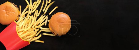 Foto de Comida rápida, vista superior. Papas fritas en un paquete mediano y hamburguesas con queso sobre un fondo de madera oscura - Imagen libre de derechos