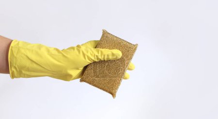 Die Hand einer Frau in einem Latexhandschuh hält einen Schwammschaber zum Waschen von Teflonoberflächen. Professionelle Reinigung. Haushaltshandschuhe, gelb. Putzfrau