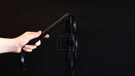 Photo for A woman's hand holds a whip against a dark background. Leather whip for spanking isolated on black. Sex toy for intimacy. Sexual slavery - Royalty Free Image