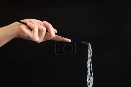 Photo for Hand holds a decorative whip with metal balls on a dark background. Sex accessory in a woman's hand. Sex toys, sex shop concept - Royalty Free Image