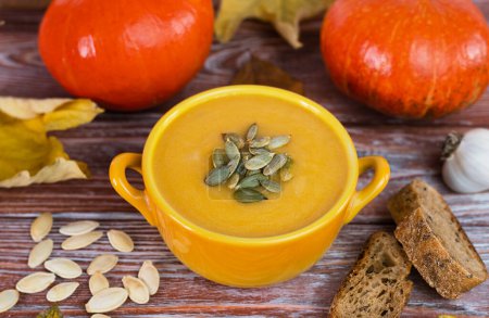 Photo for Seasonal food. Pumpkin cream soup and homemade rye bread on a wooden table. Close-up. Selective focus. - Royalty Free Image
