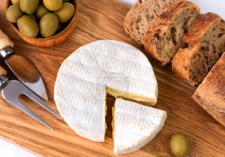Photo for Camembert cheese, fresh baguette, olives on a wooden board. Top view. Close-up. Selective focus. - Royalty Free Image
