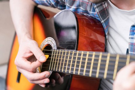 Photo for Hands of a young man with mediator playing on guitar strings. Close-up. Selective focus. - Royalty Free Image
