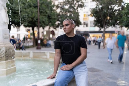 Téléchargez les photos : Une personne non binaire assise près d'une fontaine d'eau extérieure. Concept LGBTIQ. - en image libre de droit