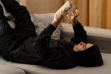 Téléchargez les photos : Adolescent lisant une bande dessinée allongée sur le canapé à la maison. Concept de loisirs et de temps libre. - en image libre de droit