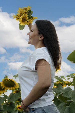Téléchargez les photos : Concept Ukraine. un symbole de paix. Une belle et heureuse fille européenne se tient dans un champ de tournesols jaunes, contre un ciel bleu, levant la main avec un bouquet de fleurs. - en image libre de droit