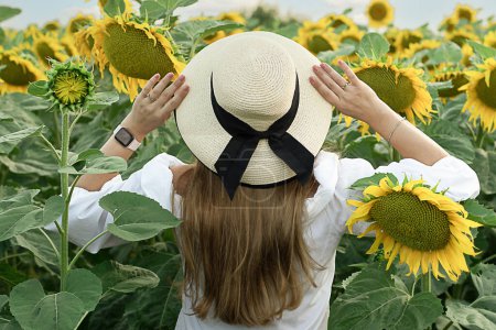 Téléchargez les photos : Un symbole de paix. Concept Ukraine. Une fille dans un chapeau de paille se tient dans un champ avec des tournesols jaunes. Vue de l'arrière. Sans visage. Gros plan. - en image libre de droit