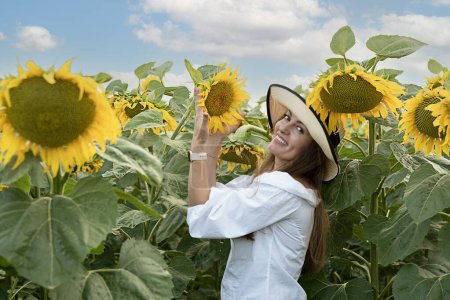 Téléchargez les photos : Une belle et heureuse fille, dans un chapeau de paille, se tient dans un champ avec des tournesols jaunes contre le ciel bleu. Concept de paix. Le symbole de l'Ukraine. Gros plan. - en image libre de droit