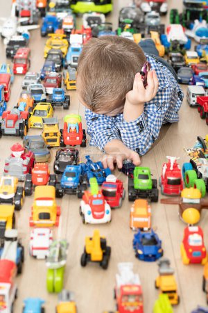 Photo for Concept of childrens toys. A little boy, 4 years old, plays happily, lying on the floor, with colorful small and large cars in the childrens room. Soft focus. - Royalty Free Image