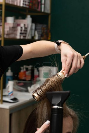 Photo for Beauty sphere. The master hairdresser does styling and combing the hair. Combs a client's long hair with a round brush and blow-dries it in a beauty salon. Close-up. Business concept. No faces. - Royalty Free Image