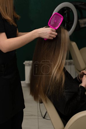 Schönheitssphäre. Der Friseurmeister frisiert und kämmt die Haare. Kämmt die langen Haare einer Kundin mit einer runden Bürste und föhnt sie in einem Schönheitssalon ab. Nahaufnahme. Geschäftskonzept.