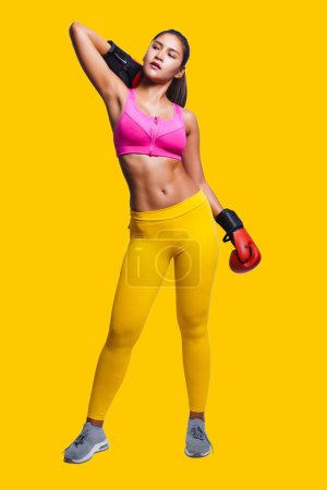 Photo for Asian woman with boxing gloves in fitness outfit while look up, isolated on yellow background. - Royalty Free Image