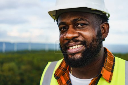 Foto de Primer plano retrato del hombre ingeniero optimista negro sonriendo y mirando al campo mientras trabaja al aire libre. - Imagen libre de derechos