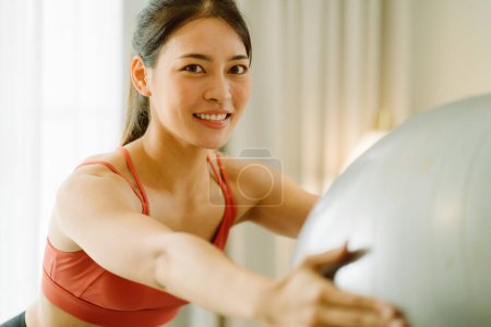 Foto de Asiático optimista c mujer con una bola de yoga en ropa deportiva sonriendo y mirando a la cámara. - Imagen libre de derechos