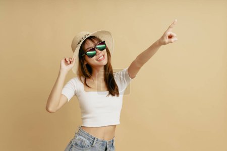 Téléchargez les photos : Portrait de femme asiatique portant des lunettes de soleil et pointant sa main vers le haut. - en image libre de droit