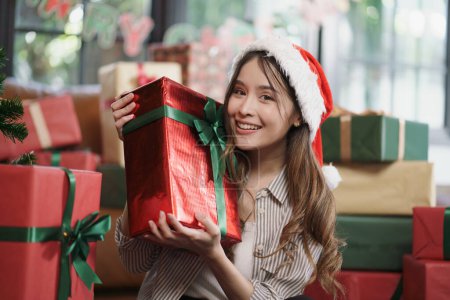 Téléchargez les photos : Femme asiatique avec boîte de cadeaux de Noël souriant à la caméra avec beaucoup de boîtes cadeaux en arrière-plan. - en image libre de droit
