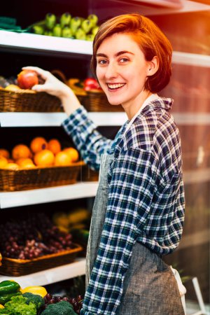 Foto de Candid Lifestyle joven hermosa mujer eligiendo fruta fresca en el estante en el supermercado. Joven hembra sin máscara en minimart. - Imagen libre de derechos