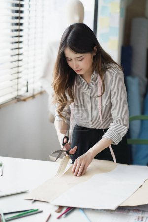 Foto de Mujer joven asiática optimista hizo su pequeño negocio como diseñador de ropa. Estilo de vida nueva generación empresaria freelancer. - Imagen libre de derechos